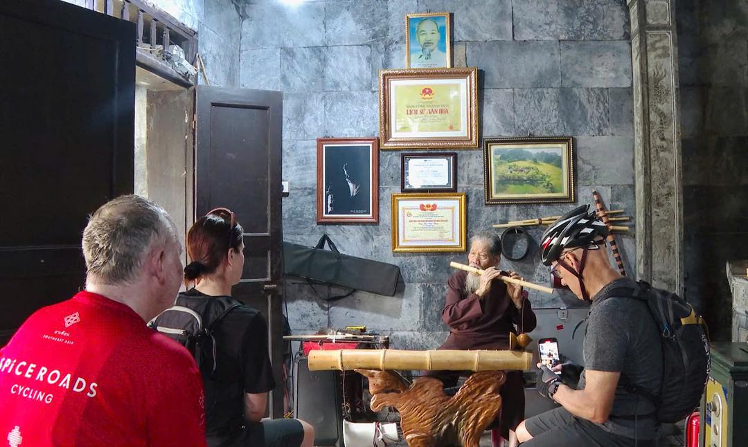 Du khách nước ngoài lắng nghe tiếng sáo trúc do cụ Chu Văn Thim biểu diễn.